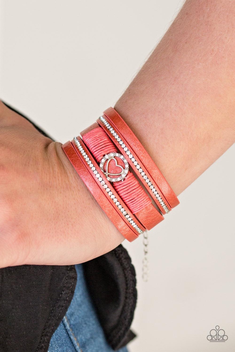 Paparazzi Accessories It Takes Heart - Orange Brushed in a metallic shimmer, strips of orange leather are encrusted in alternating rows of glittery white rhinestones. Orange cording knots around the centermost strand, securing a sparkling heart frame in p