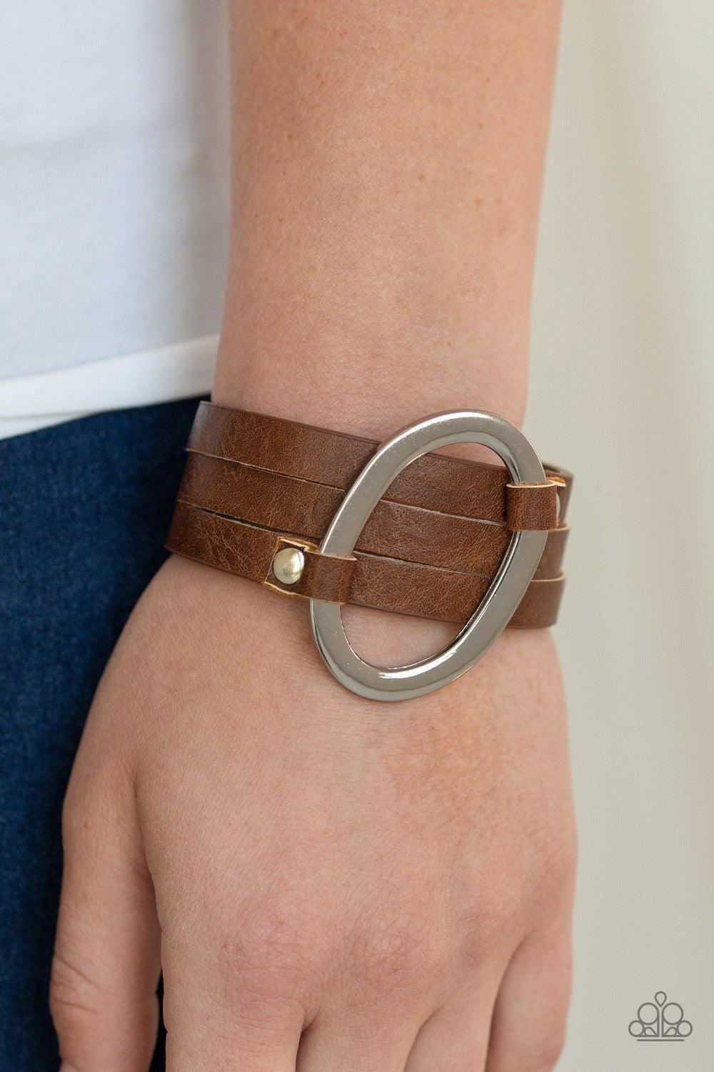 Paparazzi Accessories Cowgirl Cavalier - Brown An oval silver ring loops through two belt loop fittings and is studded in place across the front of a spliced brown leather band for a bold urban look. Features an adjustable snap closure. Jewelry