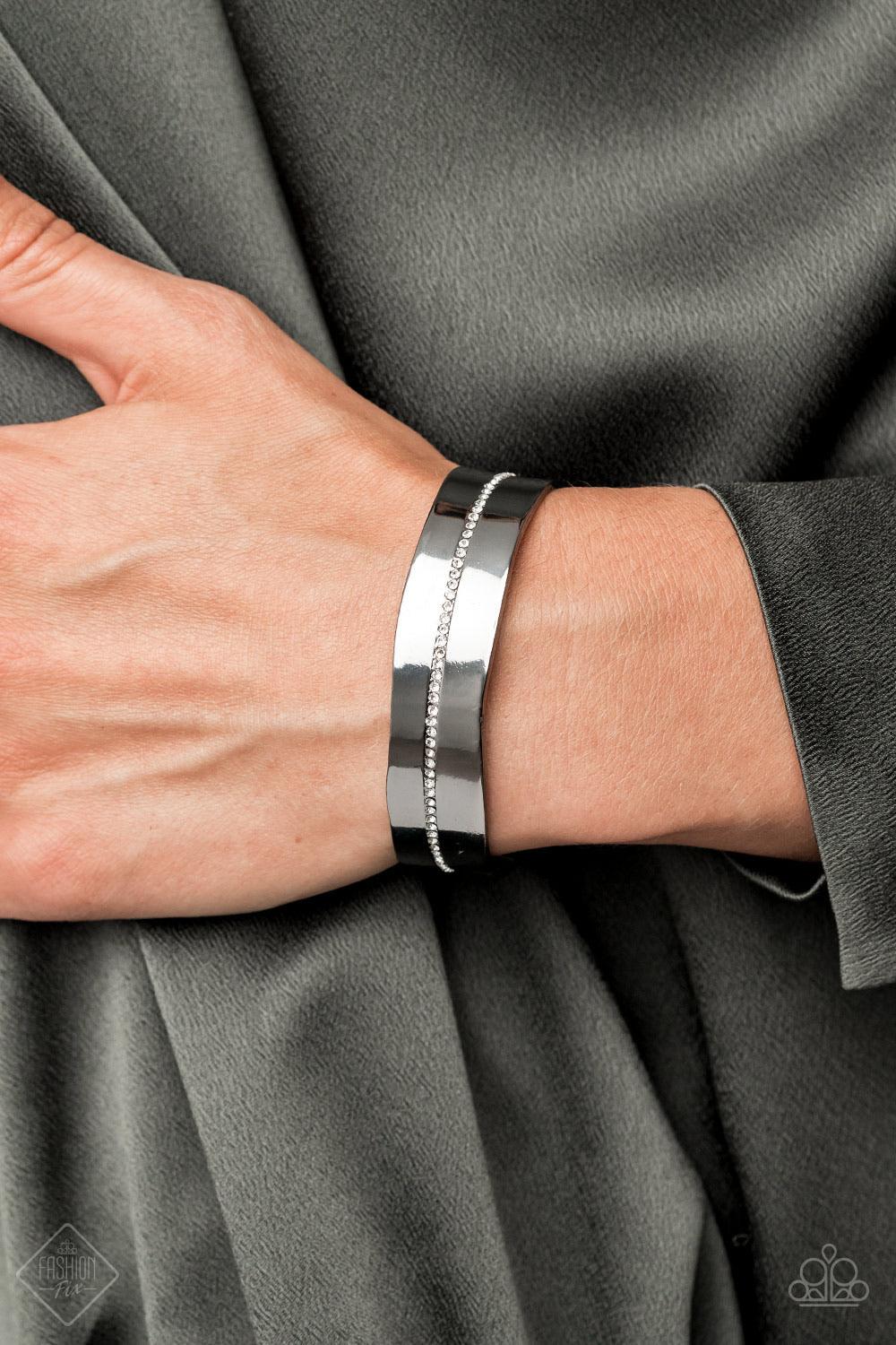 Paparazzi Accessories Raw Razzle - Black A dainty row of glassy white rhinestones is encrusted down the center of an imperfectly shaped gunmetal cuff, creating edgy shimmer around the wrist. Sold as one individual bracel Jewelry