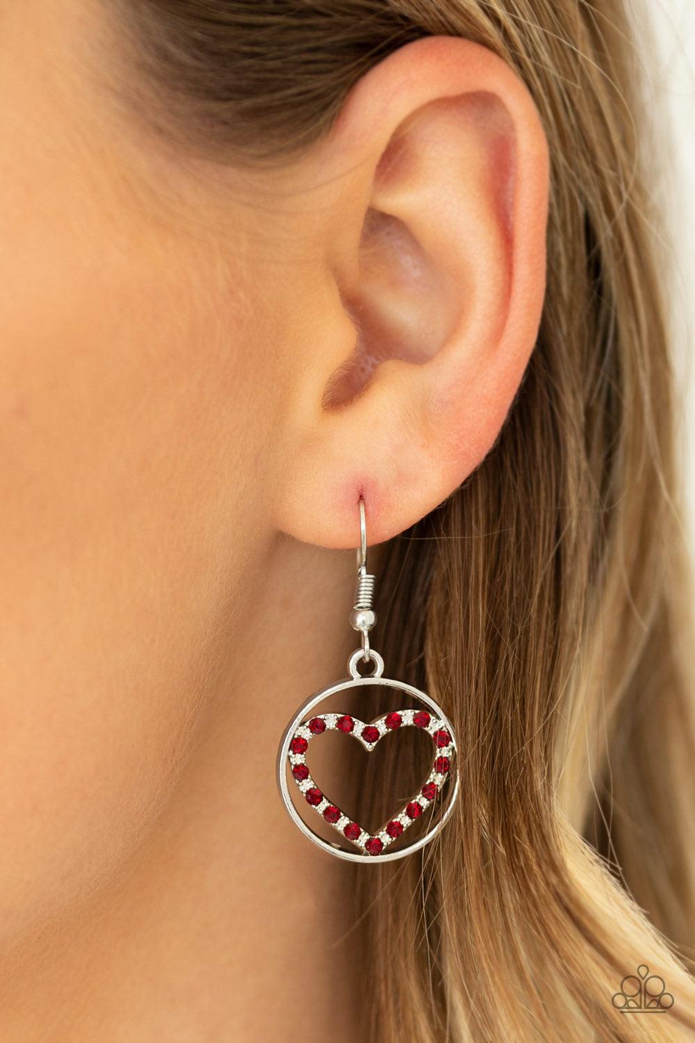 Paparazzi Accessories With My Whole Heart ~Red A red rhinestone encrusted silver heart is nestled inside a shiny silver hoop, creating a charming pendant at the bottom of an exaggerated silver chain. Features a toggle closure.