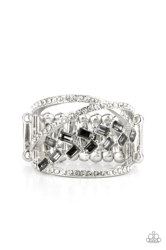 Paparazzi Accessories Lavishly Luminary - Silver Dainty silver bands of white rhinestones crisscross across the finger creating an airy frame for a trail of dainty emerald cut smoky gems that coalesce into a classic upscale finish. Features a stretchy ban