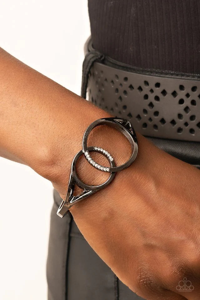 Paparazzi Accessories Scope of Experience - Black Encrusted in sections of glassy white rhinestones, two oversized gunmetal rings delicately overlap across the center of the wrist, resulting in a timeless bangle-like bracelet around the wrist. Features a