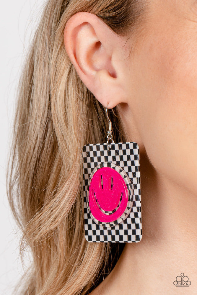 Paparazzi Accessories Cheeky Checkerboard - Pink Set against a trendy, checkerboard backdrop, an oversized, sparkly, Beetroot Purple smiley face stands out for a cheerfully captivating statement piece near the ear. Earring attaches to a standard fishhook