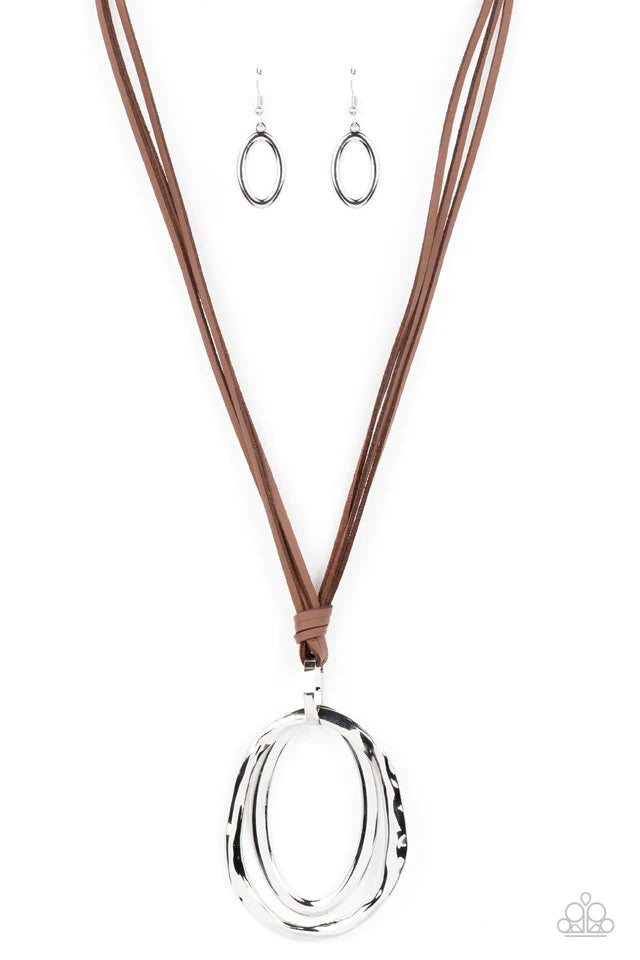 Paparazzi Accessories Long OVAL-due - Brown Long strips of brown leather knot around a silver link where a mismatched pair of smooth and hammered silver ovals swing from the bottom, resulting in a rustic pendant. Features an adjustable clasp closure. Jewe