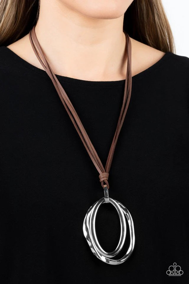 Paparazzi Accessories Long OVAL-due - Brown Long strips of brown leather knot around a silver link where a mismatched pair of smooth and hammered silver ovals swing from the bottom, resulting in a rustic pendant. Features an adjustable clasp closure. Jewe