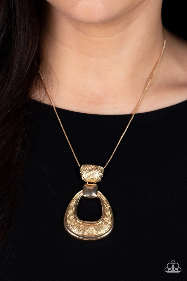 Paparazzi Accessories Park Avenue Attitude - Gold Topped with a smooth square-like accent, a hammered teardrop frame links to the bottom of a hammered gold fitting, creating a modern metallic pendant at the bottom of a rounded gold snake chain. Features a