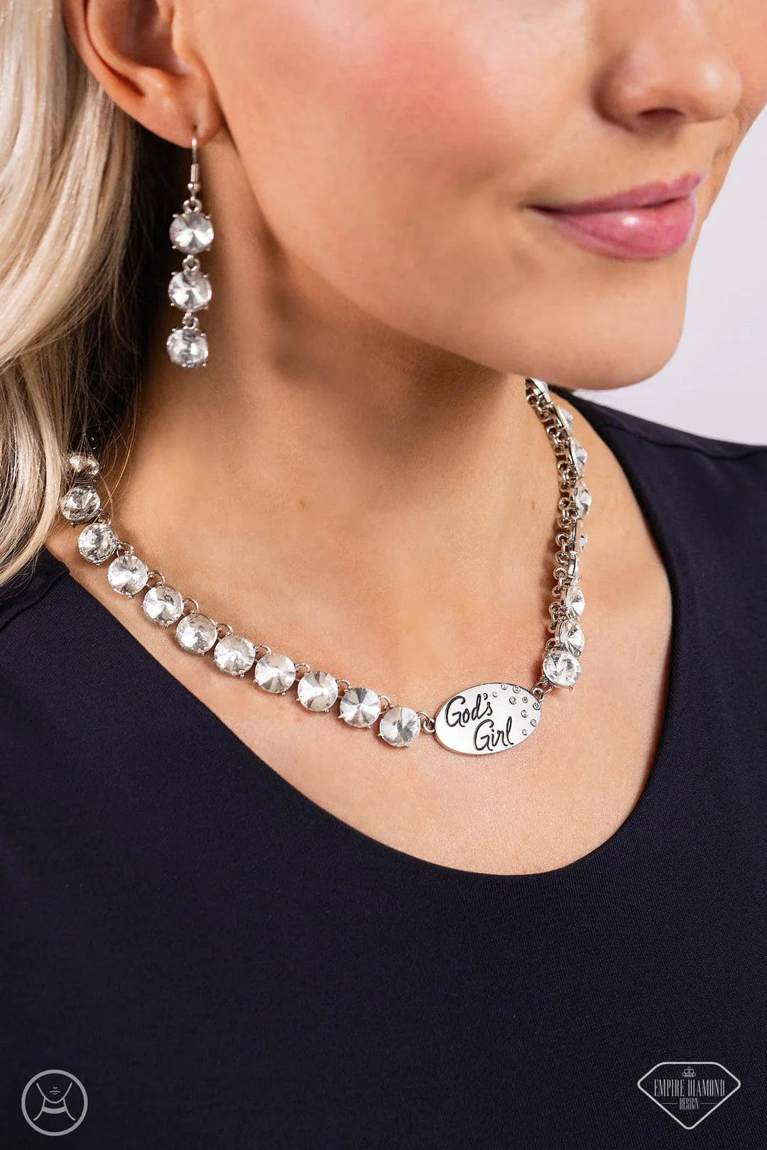 Paparazzi Accessories Gods Girl - White ! A flashy collection of oversized white gems wraps along the neckline, leading to a polished silver plate in the center. The phrase “God’s Girl” is inscribed on the metallic centerpiece in a decorative font, as a d