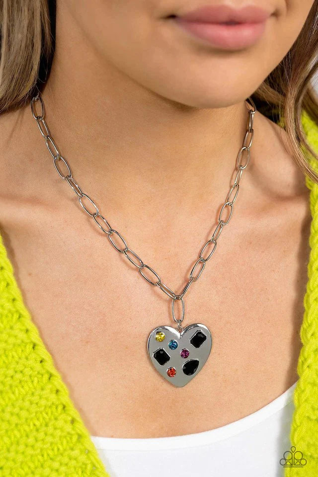 Paparazzi Accessories Online Dating - Black Falling down the neckline from a shimmery silver paperclip chain, an oversized silver heart rests for a romantic statement. Brushed with shimmery pink, yellow, orange, blue, and black gems in round, teardrop and