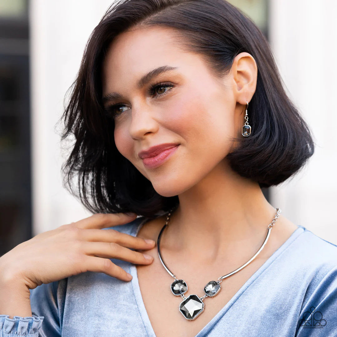 Paparazzi Accessories Divine IRIDESCENCE - Silver An oversized collection of radiant cut smoky and hematite gems delicately link at the bottom of two curved silver rods. Attached to shiny silver chains, the glamorously glitzy display sparkles below the co