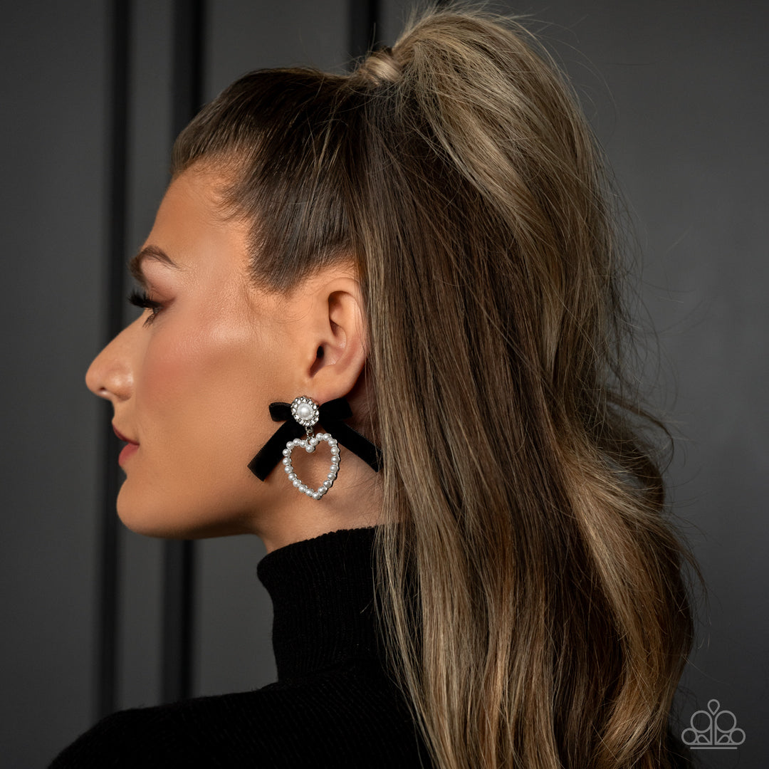 Paparazzi Accessories BOW and Then - Black A solitaire white pearl, pressed in a white rhinestone-encrusted hoop, gleams atop a pearl-dotted heart frame resulting in a dazzling statement piece. A black velvet ribbon fans out from the pearly centerpiece fu