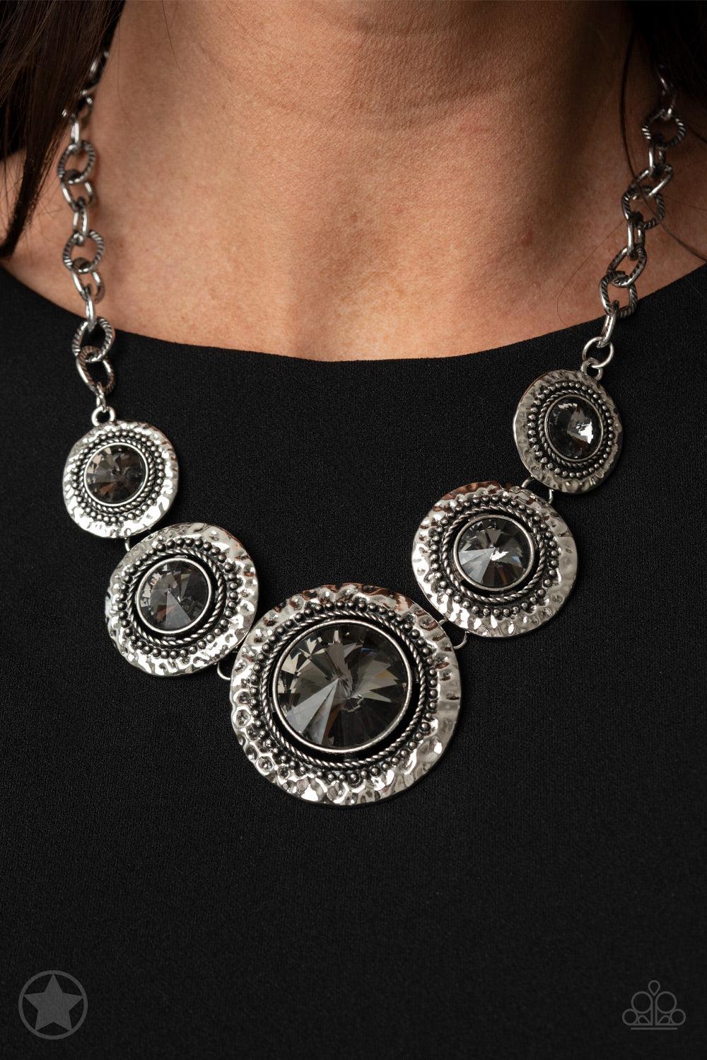 Paparazzi Accessories Global Glamour - Silver Gradually increasing in size, dramatically oversized smoky gems are pressed into the centers of hammered and silver studded frames. The blinding frames link below the collar for a glamorous, statement-making f