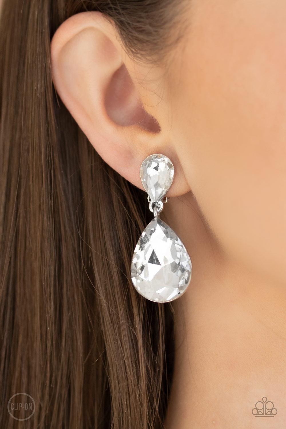 Paparazzi Accessories Aim For The MEGASTARS - White *Clip-On A dramatically oversized white rhinestone teardrop swings from the bottom of a smaller rhinestone teardrop, linking into a glamorous lure. Earring attaches to a standard clip-on fitting. Sold as
