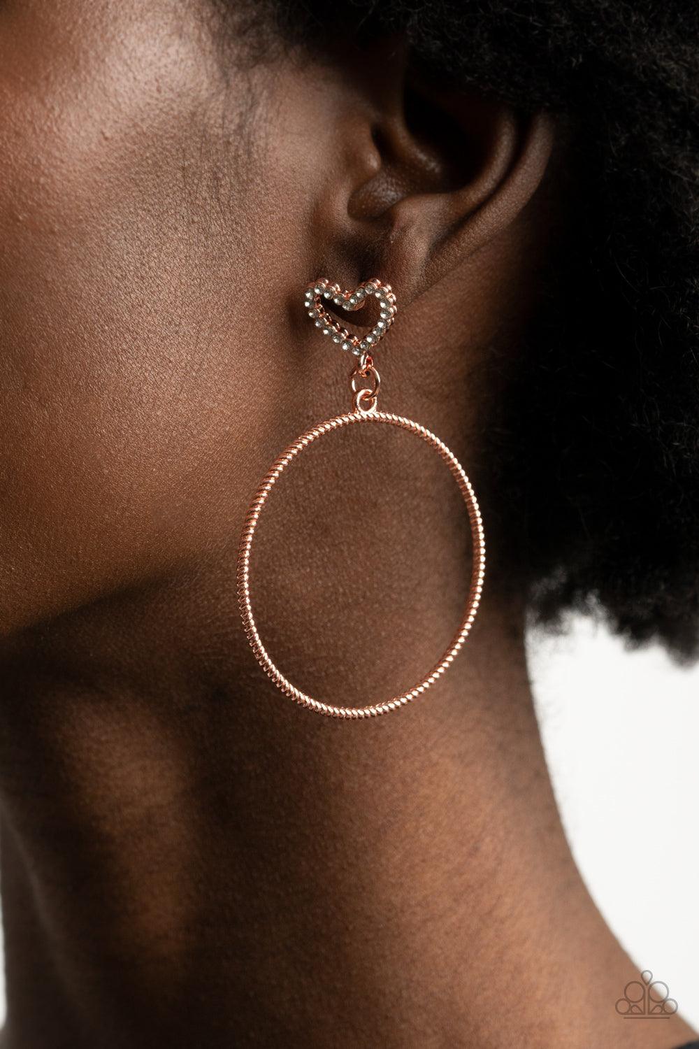 Paparazzi Accessories Love Your Curves - Copper A twisted shiny copper hoop swings from the bottom of a white rhinestone encrusted heart frame, creating a flirtatious statement piece. Earring attaches to a standard post fitting. Sold as one pair of post e