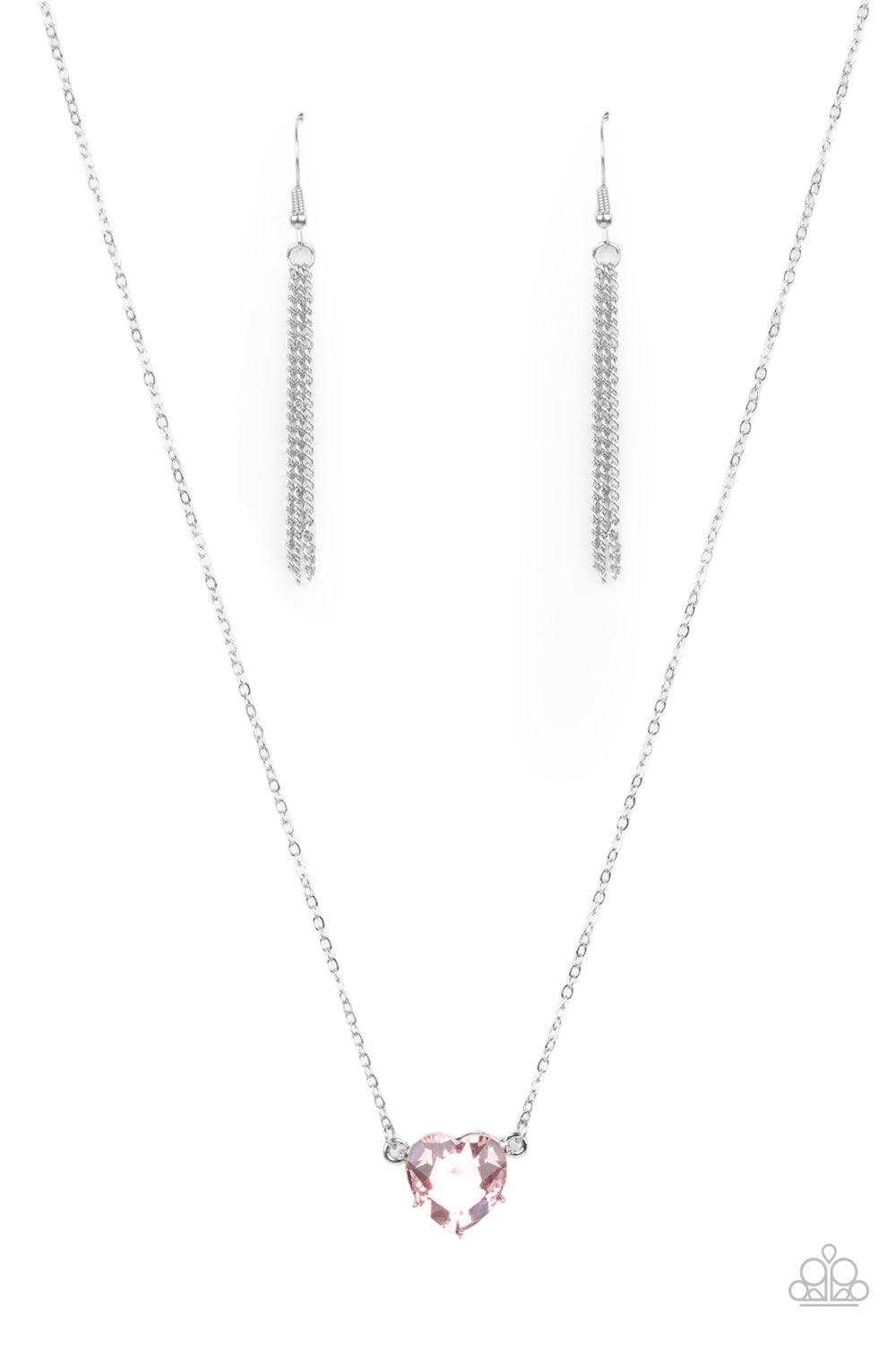 Paparazzi Accessories She Works HEART For The Money - Pink Cut into a flirtatious heart shape, a dramatically oversized pink rhinestone pendant swings from the bottom of a dainty silver chain below the collar for a glamorous finish. Features an adjustable