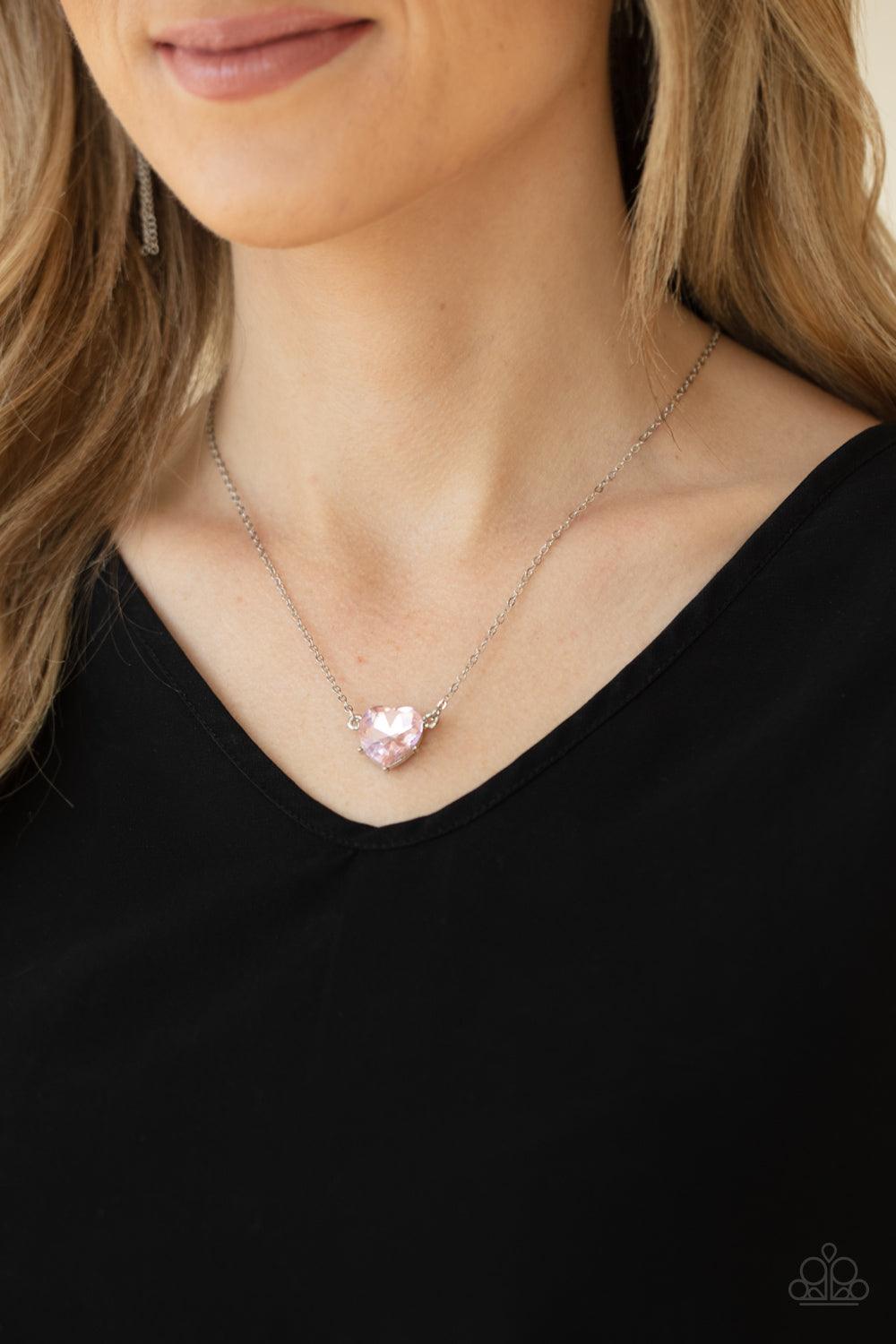 Paparazzi Accessories She Works HEART For The Money - Pink Cut into a flirtatious heart shape, a dramatically oversized pink rhinestone pendant swings from the bottom of a dainty silver chain below the collar for a glamorous finish. Features an adjustable
