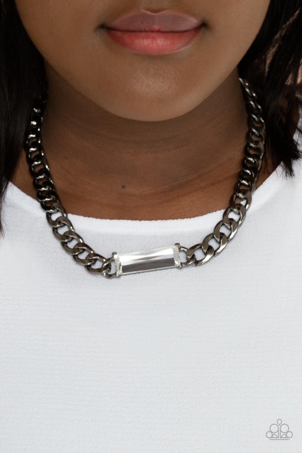 Paparazzi Accessories Urban Royalty - Black A dramatically oversized row of gunmetal chain attaches to a white emerald cut rhinestone pendant, creating a demanding centerpiece below the collar. Features an adjustable clasp closure. Sold as one individual