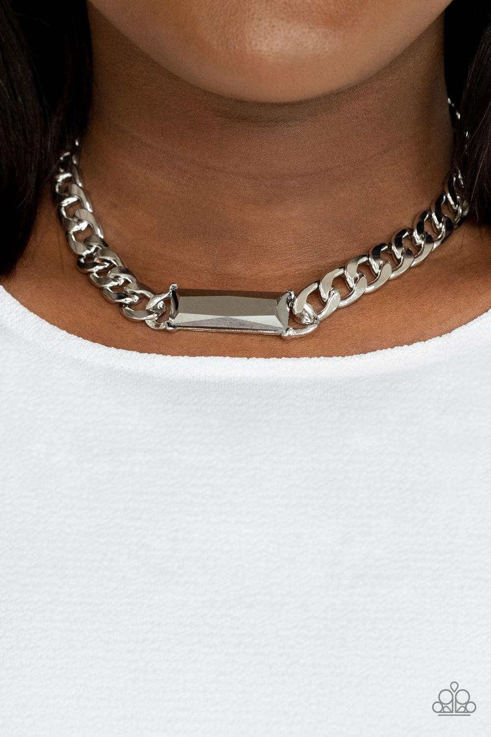 Paparazzi Accessories Urban Royalty - Silver A dramatically oversized row of silver chain attaches to an emerald cut hematite rhinestone pendant, creating a demanding centerpiece below the collar. Features an adjustable clasp closure. Sold as one individu