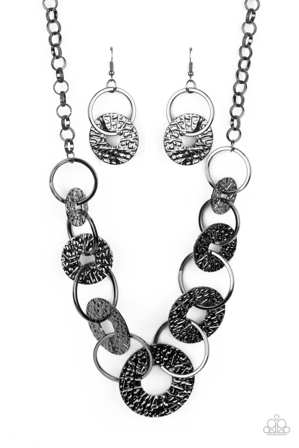 Paparazzi Accessories Industrial Envy - Black Gradually increasing in size near the center, a collection of glistening gunmetal rings and abstract hammered discs interlock below the collar for an intense industrial look. Features an adjustable clasp closu