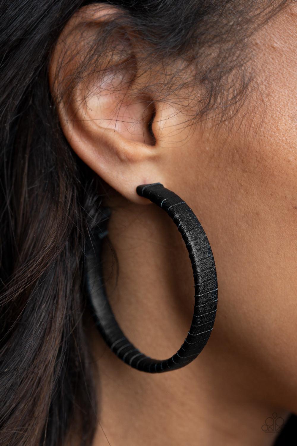 Paparazzi Accessories Leather-Clad Legend - Black A black leather lace wraps around a thick silver hoop, creating an edgy display. Earring attaches to a standard post fitting. Hoop measures approximately 2 1/2" in diameter. Sold as one pair of hoop earrin