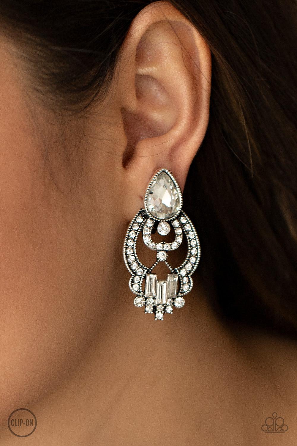 Paparazzi Accessories Glamour Gauntlet - White *Clip-On An oversized white teardrop gem and dainty row of white emerald cut rhinestones adorn a regal white rhinestone encrusted frame, creating a royal statement piece. Earring attaches to a standard clip-o