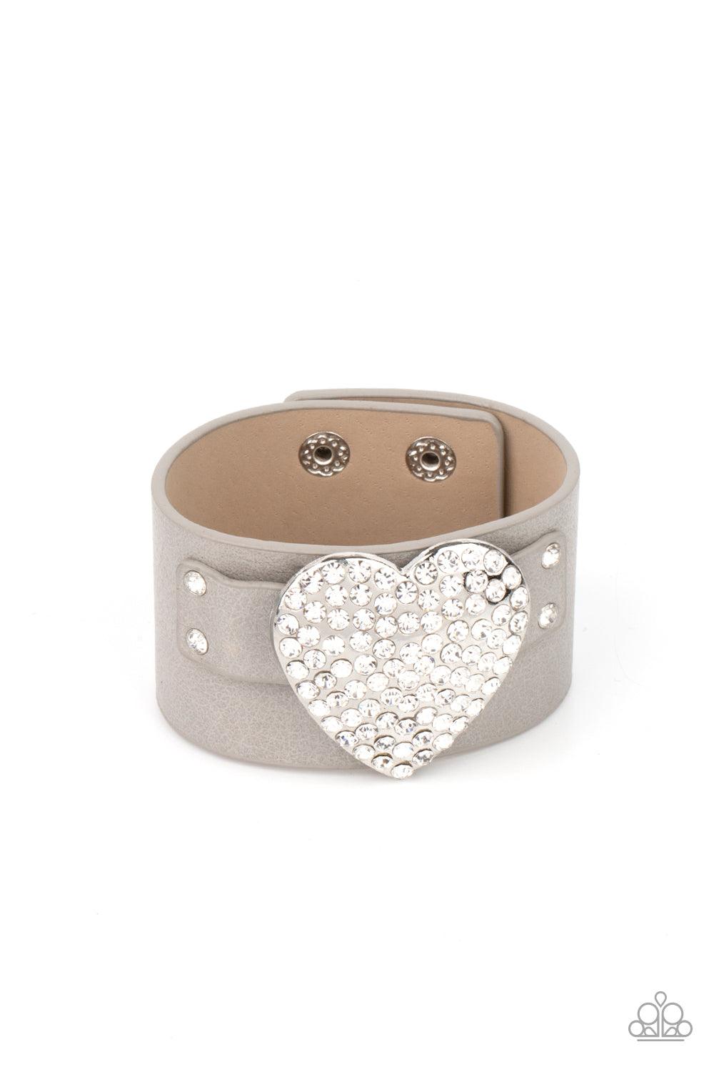 Paparazzi Accessories Flauntable Flirt - Silver Encrusted in blinding white rhinestones, an oversized silver heart frame is studded in place across the front of a gray leather band, creating a flirtatious centerpiece around the wrist. Features an adjustab