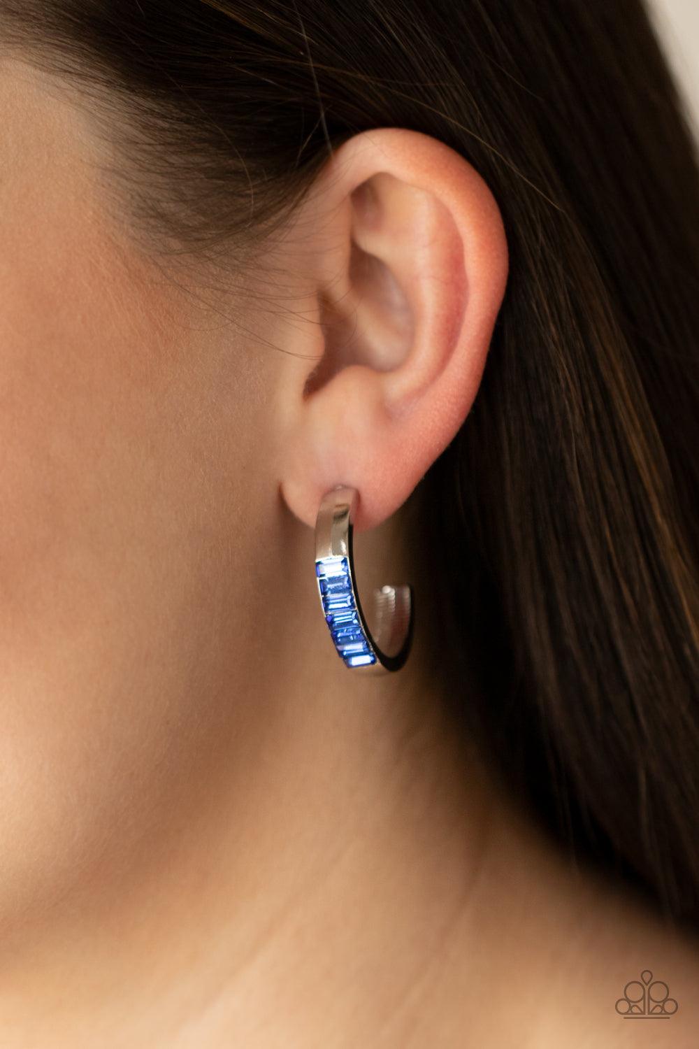 Paparazzi Accessories Bursting With Brilliance - Blue The front of a thick silver hoop is encrusted in glittery blue emerald cut rhinestones, creating a glamorous pop of color. Earring attaches to a standard post fitting. Hoop measures approximately 1" in