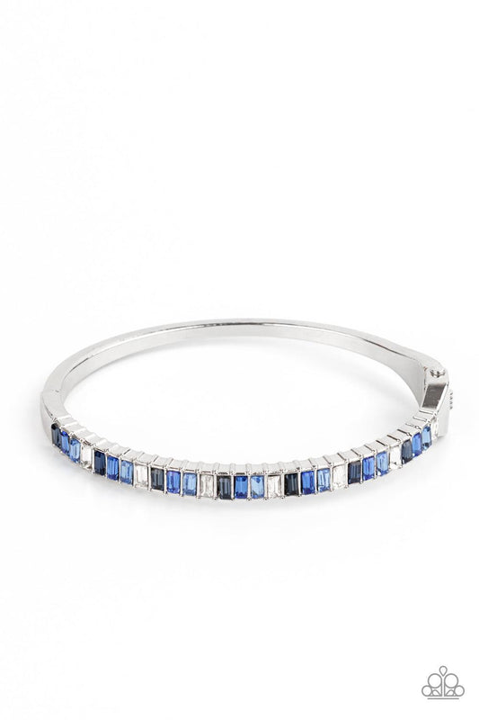 Paparazzi Accessories Toast to Twinkle - Blue Featuring regal emerald style cuts, a dainty row of blue and white rhinestones are encrusted across the front of a silver cuff-like bangle for a timeless fashion. Features a hinged closure. Sold as one individ
