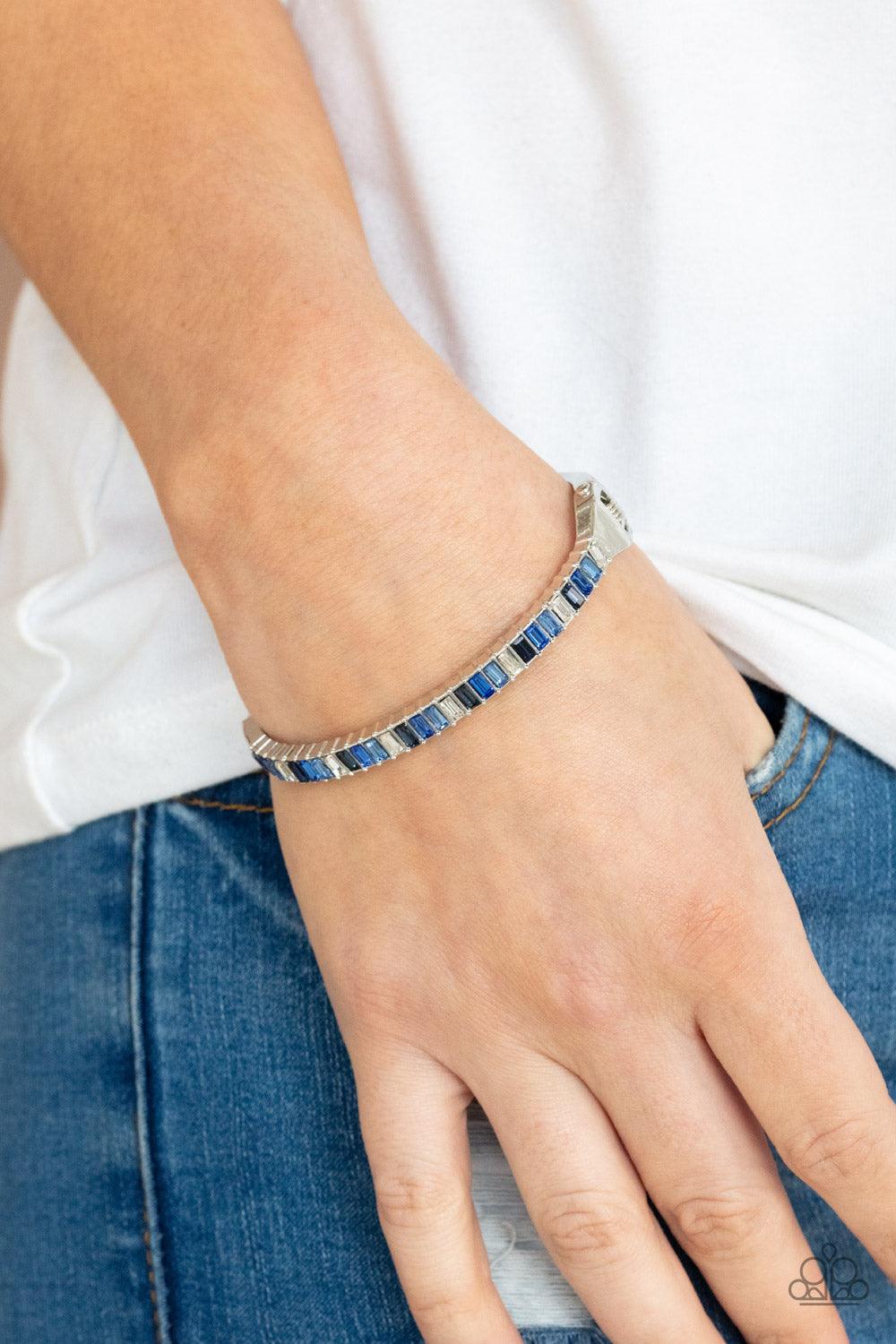 Paparazzi Accessories Toast to Twinkle - Blue Featuring regal emerald style cuts, a dainty row of blue and white rhinestones are encrusted across the front of a silver cuff-like bangle for a timeless fashion. Features a hinged closure. Sold as one individ