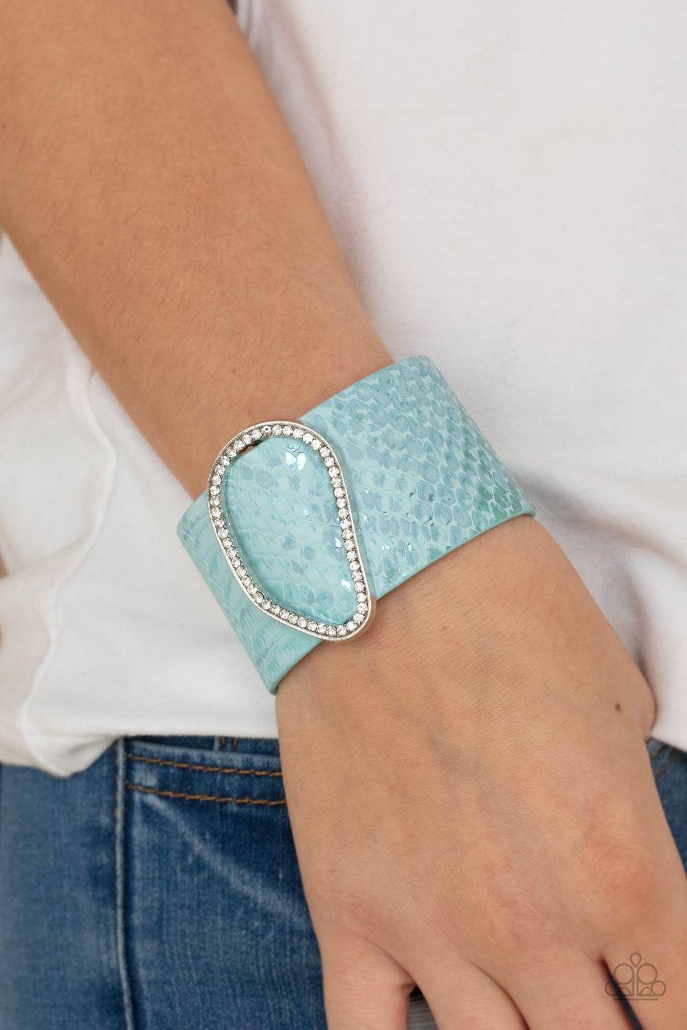 Paparazzi Accessories HISS-tory In The Making - Blue Encrusted with glassy white rhinestones, an asymmetrical silver fitting glides along a blue leather band adorned in a metallic python print for a wild look. Features an adjustable snap closure. Sold as