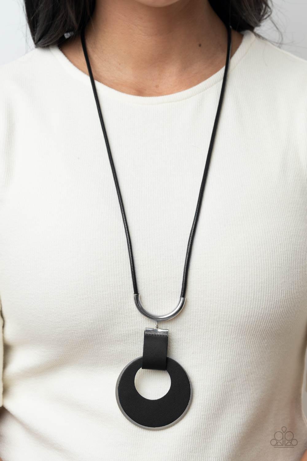 Paparazzi Accessories Luxe Crush - Black A large cutout silver disc, overlaid with black leather, is cradled in a wide black leather strap. The luxe pendant sways from a U-shaped silver cylinder threaded along the end of a lengthened polished black cord f