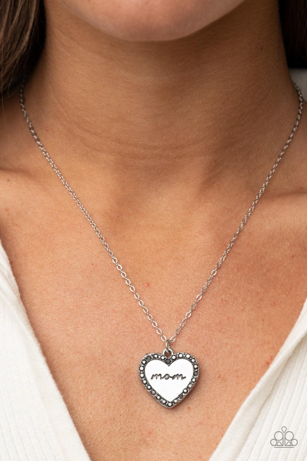 Paparazzi Accessories The Real Boss - Silver Infused with a smoky hematite rhinestone encrusted silver heart, a silver heart shaped pendant is stamped in the word, "Mom," as it swings below the collar, creating a sparkly sentimental statement piece. Featu