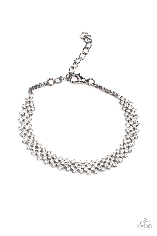 Paparazzi Accessories Chicly Candescent - Black Featuring sleek gunmetal fittings, dainty rows of glassy white rhinestones delicately slant across the wrist, coalescing into a timeless centerpiece. Features an adjustable clasp closure. Sold as one individ