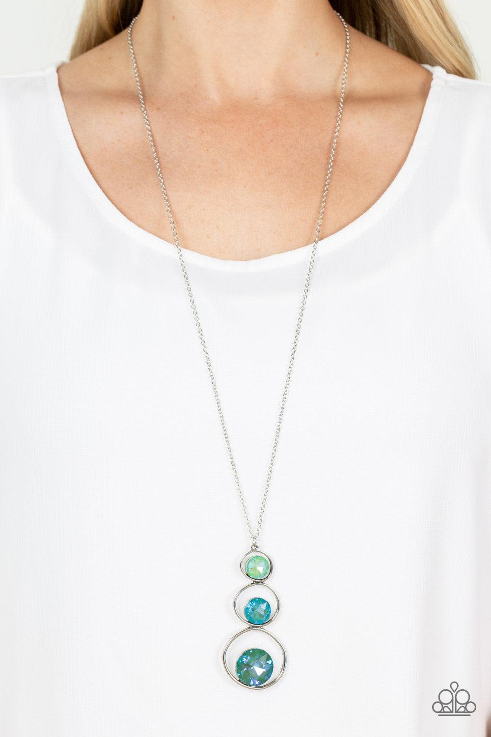 Paparazzi Accessories Celestial Courtier - Green A sparkly ombré of opalescent green gems adorn the bottoms of three silver hoops that gradually increase in size as they stack into an asymmetrical pendant. The glowing pendant swings from the bottom of a l