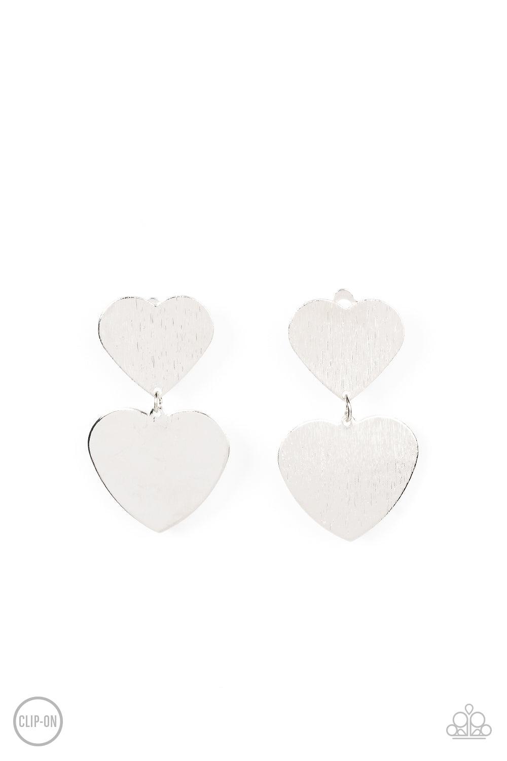 Paparazzi Accessories Cowgirl Crush - Silver *Clip-On Featuring a shimmery scratched finish, an oversized silver heart charm swings from the bottom of a smaller silver heart charm, resulting in a flirtatious lure. Earring attaches to a standard clip-on fi