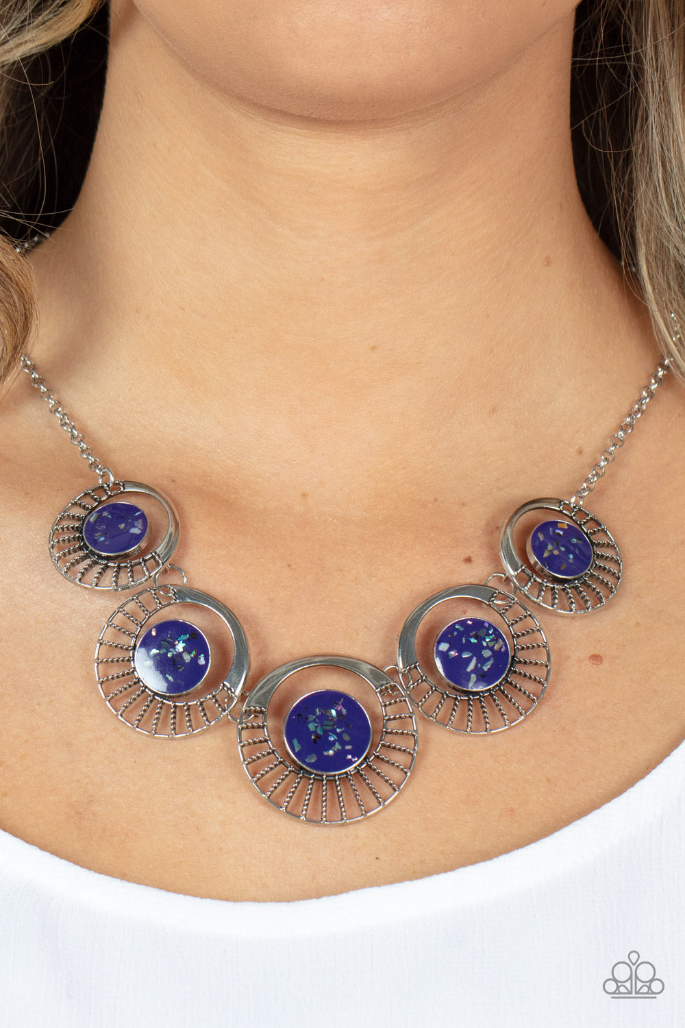 Paparazzi Accessories Elliptical Effervescence - Purple Flecked with shell-like accents, shiny purple frames adorn the centers of circulating silver frames below the collar. Featuring studded silver spokes that flair out from the bottom, the colorful fram