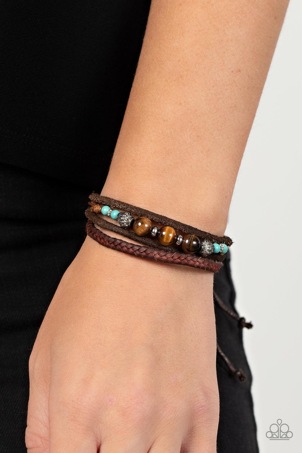 Paparazzi Accessories Tundra Tracker - Blue A strand of Tiger's eye stones, turquoise accents, and decorative silver beads join layers of mismatched leather bands around the wrist for a groovy grounding effect. Features an adjustable sliding knot closure.