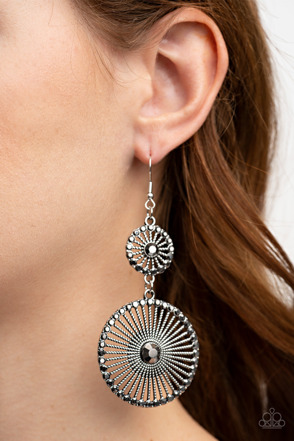 Paparazzi Accessories Bring Down the WHEELHOUSE - Silver Bordered in dainty hematite rhinestones and adorned with oversized hematite rhinestone centers, a pair of silver frames radiating with textured silver spokes links into a dizzying lure for an edgy s