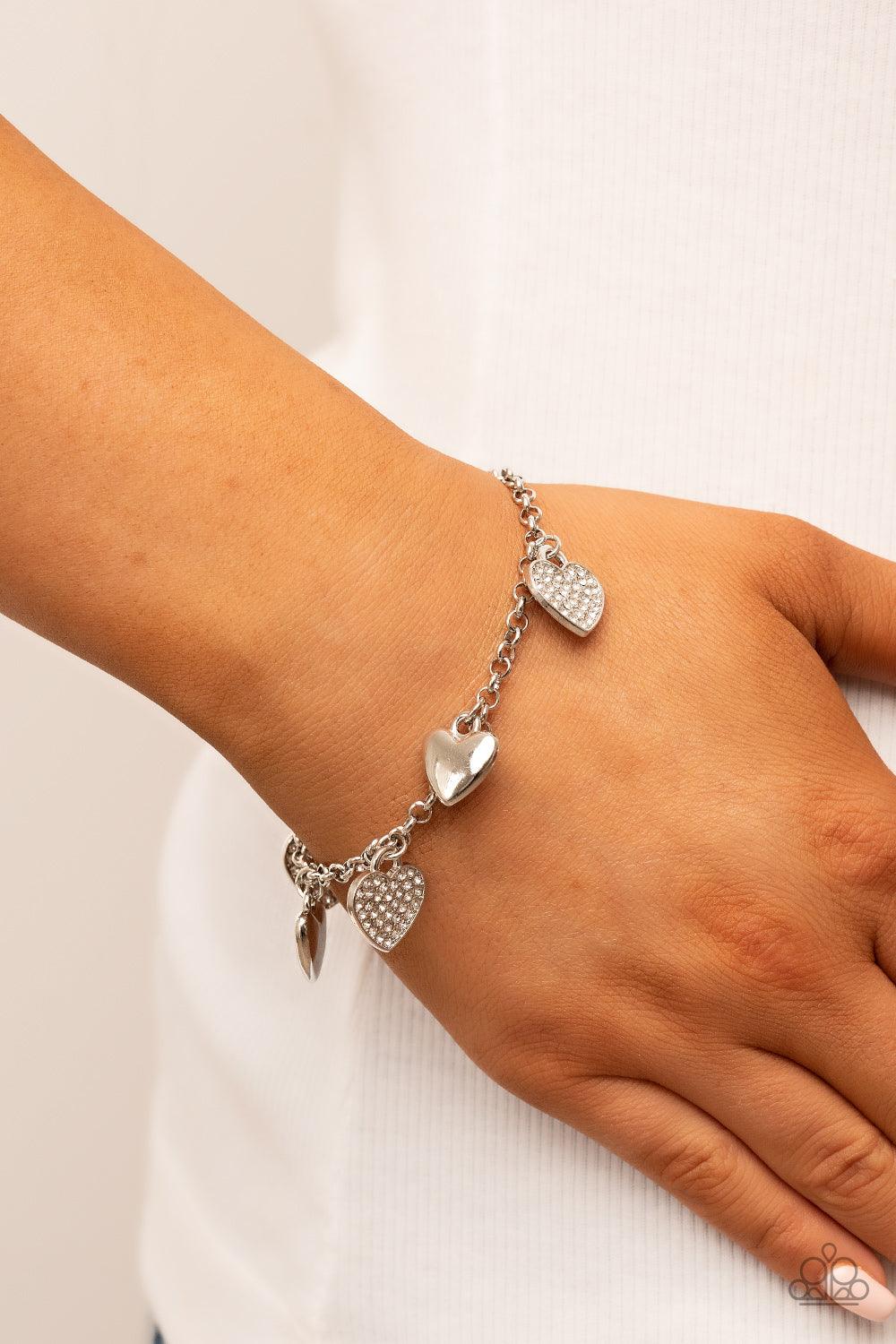 Paparazzi Accessories Lusty Lockets - White Shiny silver heart charms delicately alternate with white rhinestone encrusted heart frames along a silver chain around the wrist, resulting in a flirtatious fringe. Features an adjustable clasp closure. Sold as