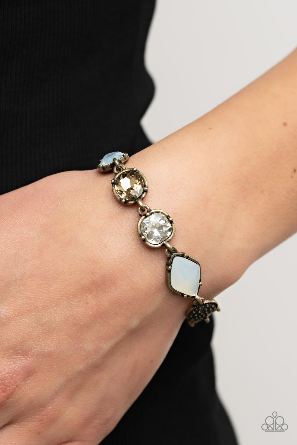 Paparazzi Accessories Jewelry Box Bauble - Brass Encased in pronged brass fittings, a mismatched collection of brassy, white, and opal rhinestones delicately links with a studded brass frame around the wrist for a sentimental sparkle. Features an adjustab