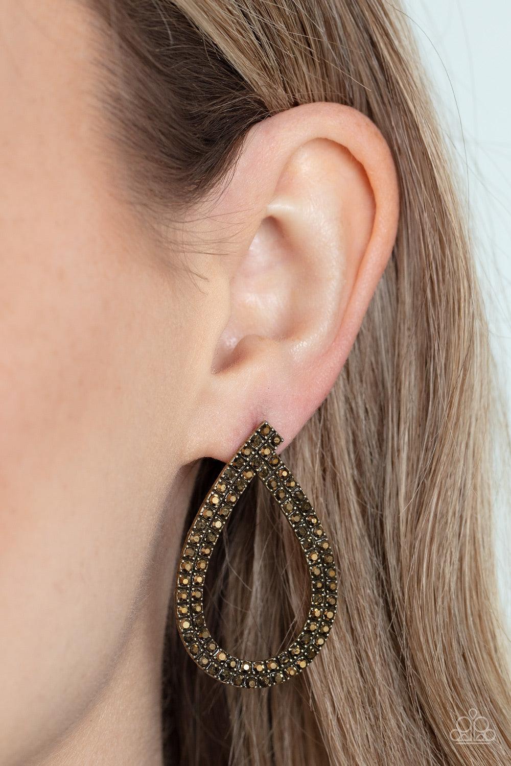 Paparazzi Accessories Diva Dust - Brass Glitzy ribbons of dainty aurum rhinestones delicately swoop into a gritty teardrop frame, resulting in a sultry sparkle. Earring attaches to a standard post fitting. Sold as one pair of post earrings. Earrings