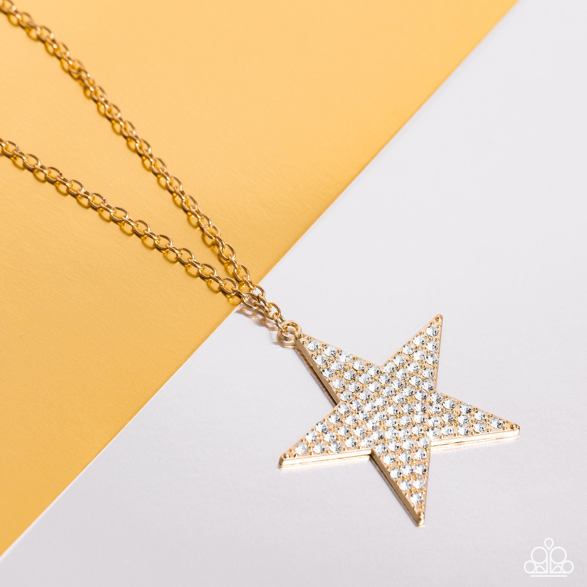 Paparazzi Accessories Rock Star Sparkle - Gold The front of an oversized gold star is encrusted in blinding white rhinestones, resulting in a stellar pendant at the bottom of a lengthened gold chain. Features an adjustable clasp closure. Sold as one indiv