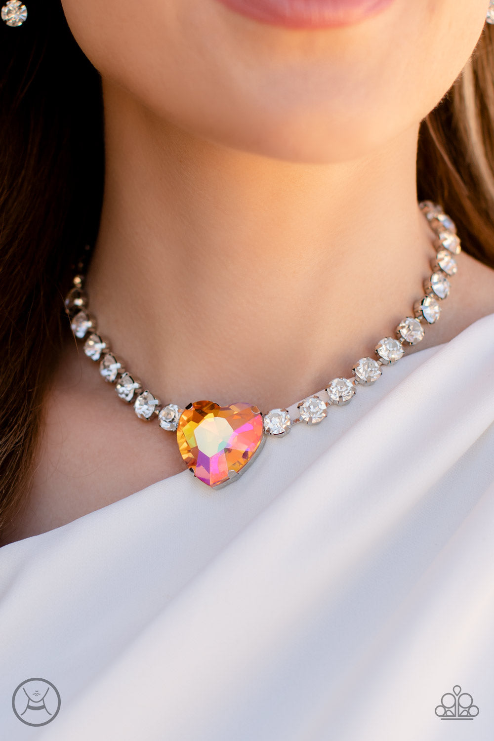 Paparazzi Accessories Heart in My Throat - Orange A dramatically oversized heart-shaped gem with a reflective, iridescent orange finish glitters at the center of a blinding row of glassy white rhinestones, resulting in a flirtatious sparkle around the nec