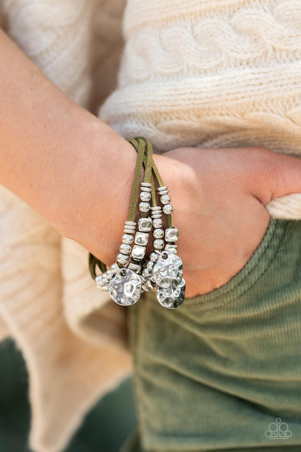 Paparazzi Accessories Token Trek - Green Asymmetrical, hammered silver discs swing from layers of Martini Olive suede that are adorned with silver discs, beads, and cubes, resulting in noisemaking shimmer around the wrist. Features an adjustable clasp clo