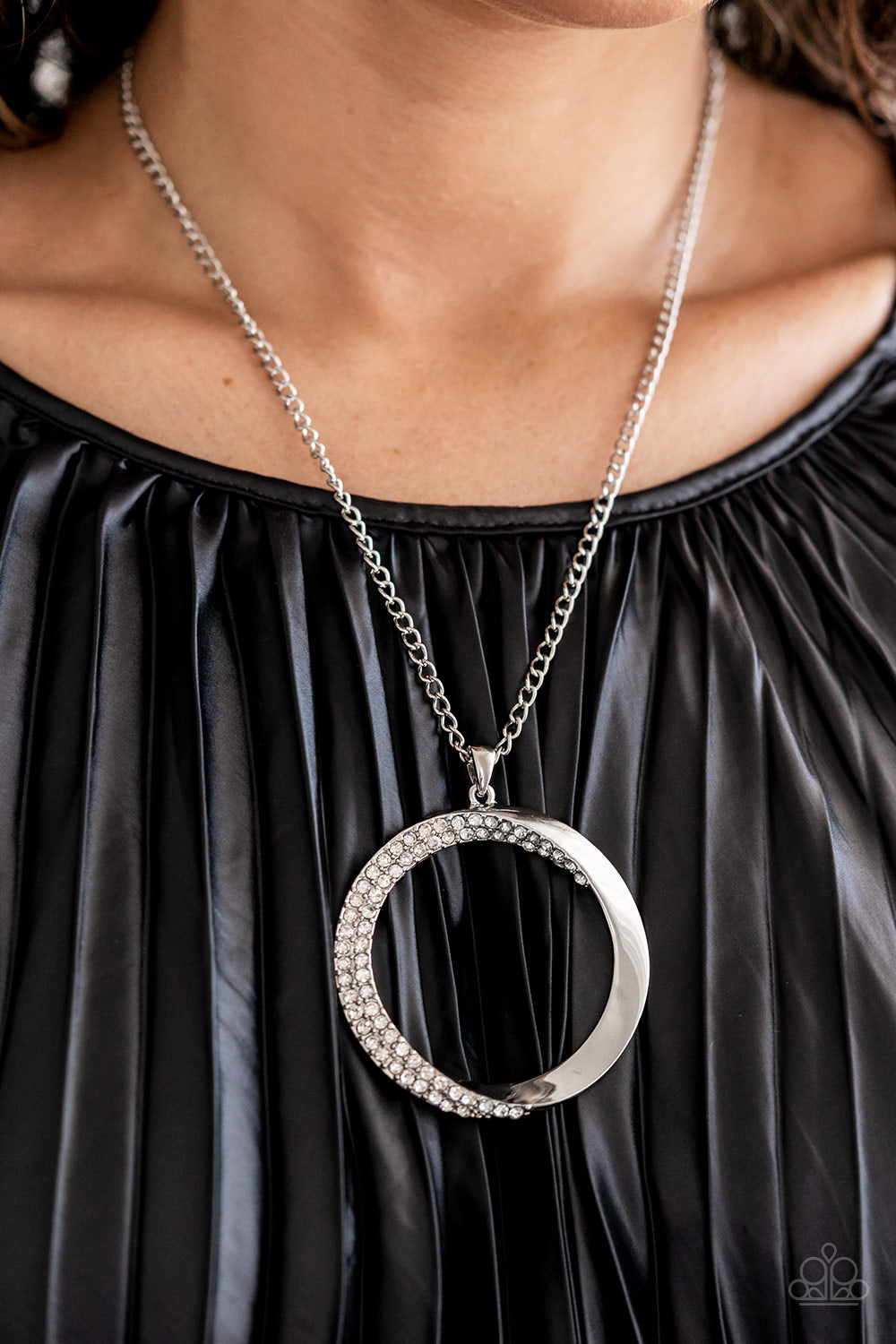 Paparazzi Accessories Encrusted Elegance - White An airy, oversized, warped, shiny silver hoop dangles down the chest from a classic silver chain. Two rows of dainty white rhinestones encrust along the inner curve of the hoop for an understated, elegant d