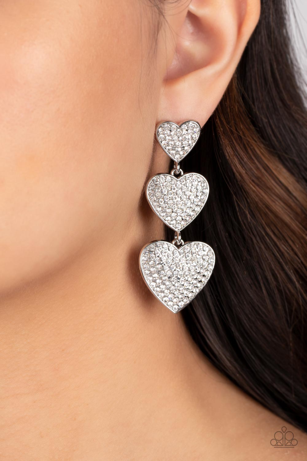 Paparazzi Accessories Couples Retreat - White Three white rhinestone-studded silver hearts gradually increase in size as they cascade down the ear in a shimmery display. Each of the hearts interconnect to one another adding a shifting, whimsical detail to