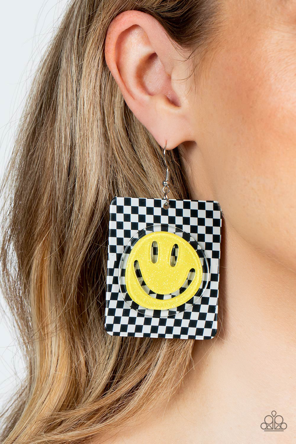 Paparazzi Accessories Cheeky Checkerboard - Yellow Set against a trendy, checkerboard backdrop, an oversized, sparkly, yellow smiley face stands out for a cheerfully captivating statement piece near the ear. Earring attaches to a standard fishhook fitting