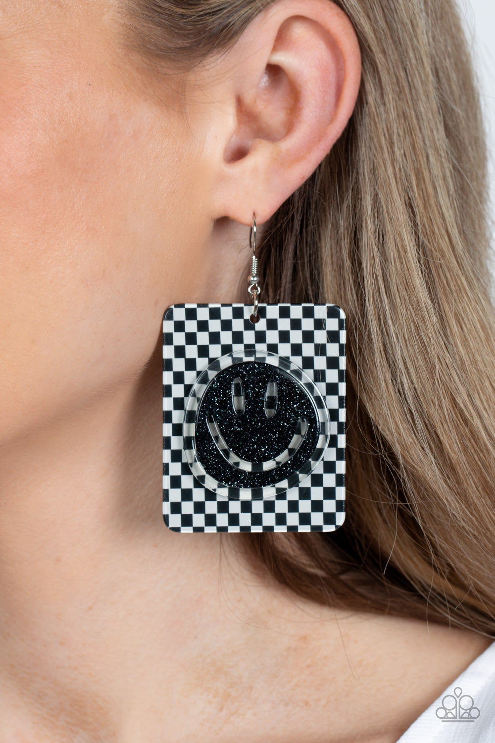 Paparazzi Accessories Cheeky Checkerboard - Black Set against a trendy, checkerboard backdrop, an oversized, sparkly, black smiley face stands out for a cheerfully captivating statement piece near the ear. Earring attaches to a standard fishhook fitting.