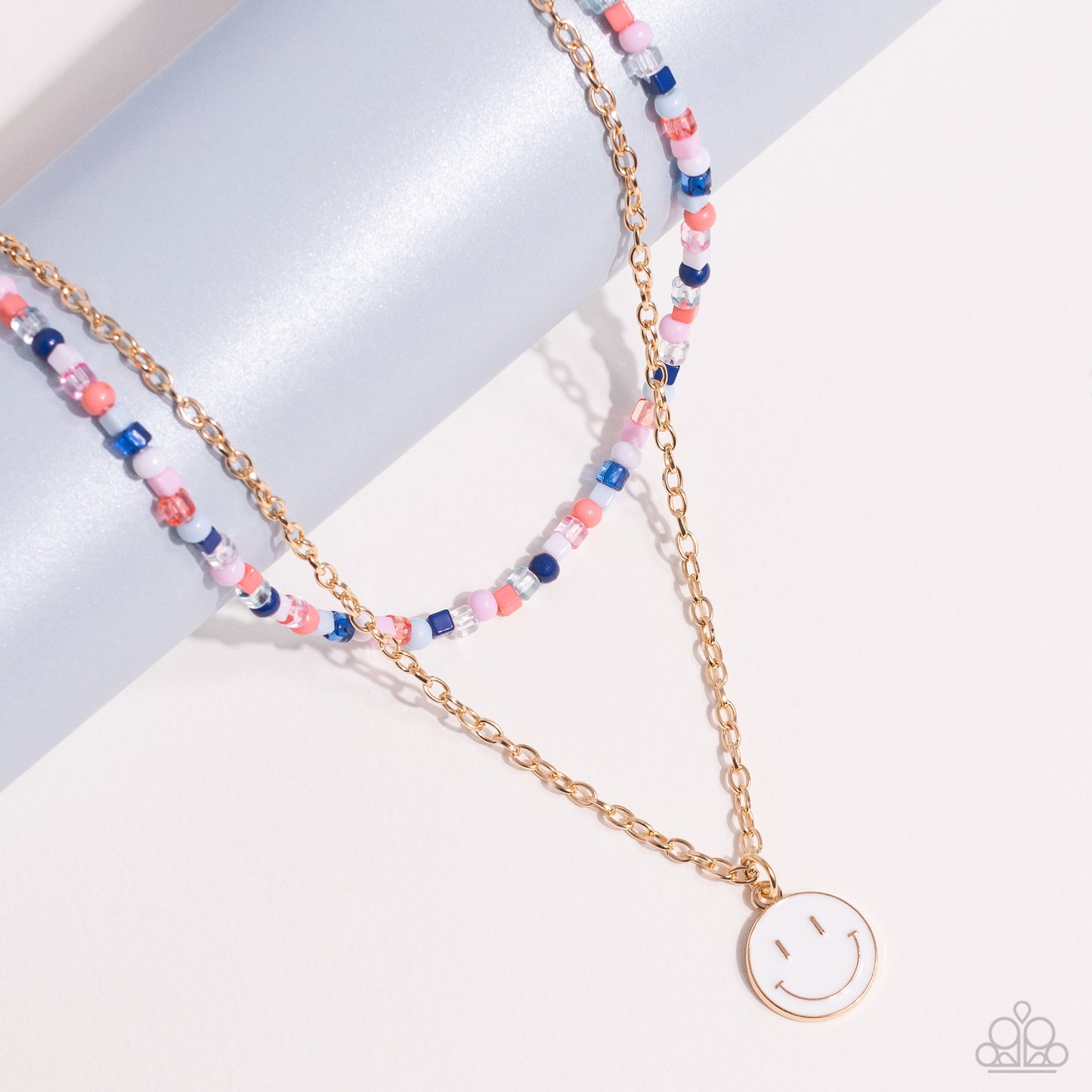Paparazzi Accessories High School Reunion - Blue Gliding from a dainty, gold chain, a smiley face pendant stands out against a white backdrop. Completing the charismatic ensemble, a collection of seed beads in shades of Spun Sugar, baby pink, navy blue, w