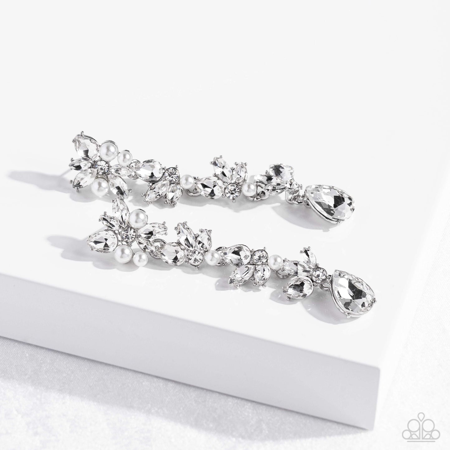 Paparazzi Accessories LIGHT at the Opera - White Radiant clusters of white reflective teardrop, marquise-cut and round gems combine with classic white pearls to create an explosion of glitz that extends down the ear. Hanging from the bottom of the light-r