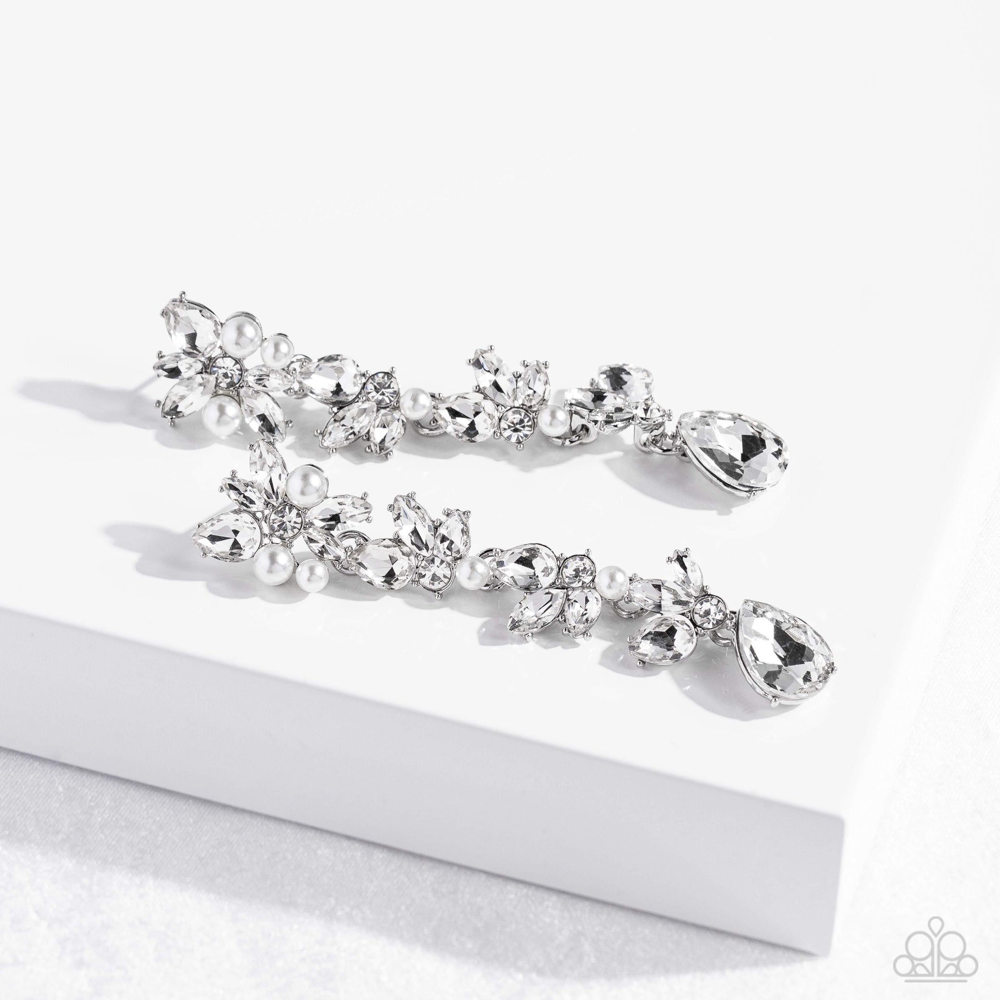 Paparazzi Accessories LIGHT at the Opera - White Radiant clusters of white reflective teardrop, marquise-cut and round gems combine with classic white pearls to create an explosion of glitz that extends down the ear. Hanging from the bottom of the light-r